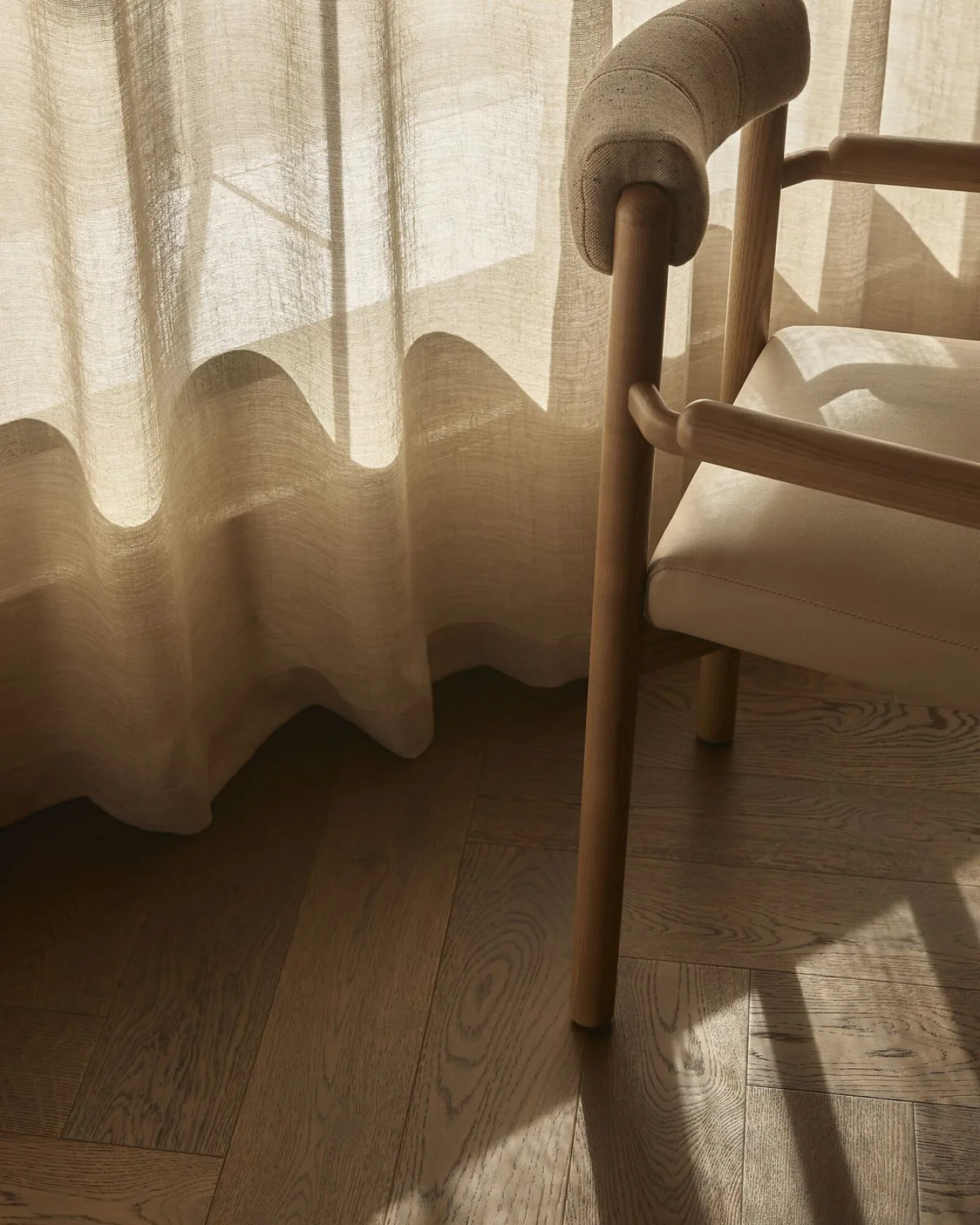 Sunlight through sheer curtains beside a wooden chair